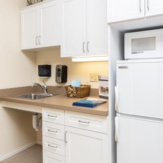 A compact kitchenette with a sink, white cabinets, and essential appliances like a refrigerator and microwave.