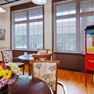 A cozy cafe interior featuring tables and chairs, a popcorn machine, and a vase of flowers by large windows.