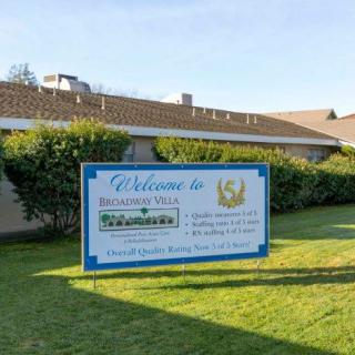 A welcoming sign in a residential neighborhood with hedges and houses in the background.