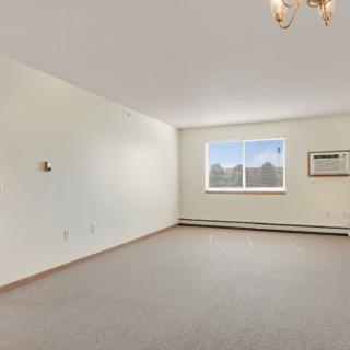 An empty living room with a window, air conditioner, and chandelier.