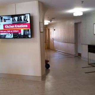 A hallway with a television displaying an advertisement for Kitchen Kreations Cafe & Catering.
