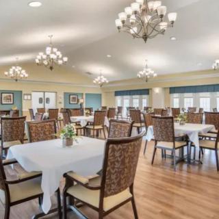 A spacious dining room with elegantly set tables, lined with chairs and adorned by chandeliers.