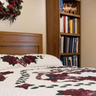 A cozy bedroom with a floral quilt and bookshelf.