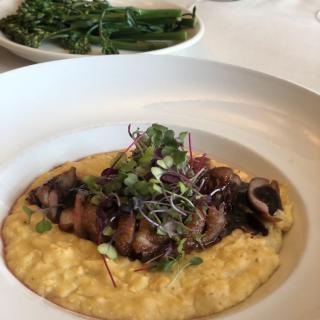 A plated dish featuring creamy mushroom risotto garnished with microgreens, accompanied by a side of steamed greens.