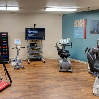 A fitness room equipped with various exercise machines including treadmills and stationary bikes, featuring a wooden floor and a television on the wall.
