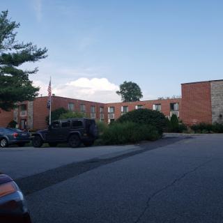 A view of an apartment complex surrounded by trees and parked vehicles under a clear blue sky.