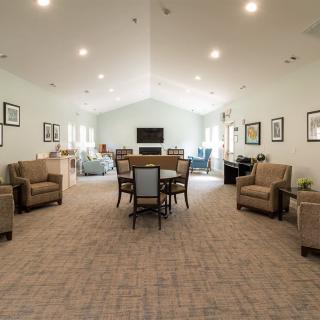 A spacious living room with arranged sofas and a central table surrounded by chairs, well-lit with ceiling lights.