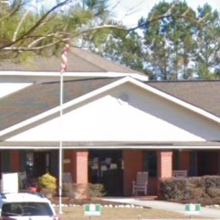 A building with a sloped roof and flagpole in front, surrounded by trees.