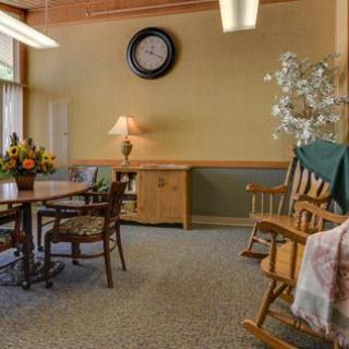 A cozy living room with a rocking chair, table with flowers, and a large wall clock.