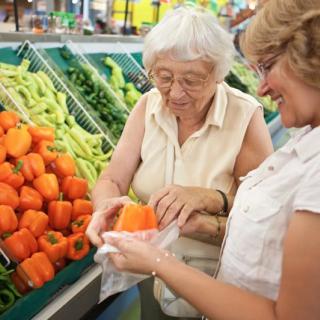 Two women selecting bell peppers in the produce section of a grocery store.