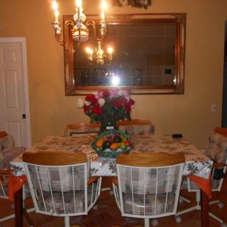 A cozy dining room with a table set for a meal, featuring a floral centerpiece and warm lighting from a chandelier.