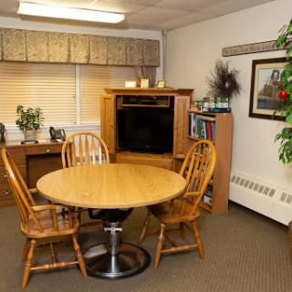 A cozy dining area featuring a round wooden table and four chairs, complemented by a TV stand and decorative plants.