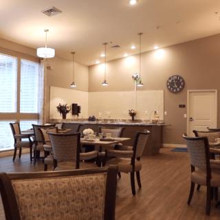 A modern dining area with wooden flooring, featuring tables and chairs, pendant lighting, and an open kitchen space.