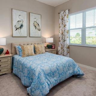 A cozy and well-decorated bedroom featuring a bed with blue bedding, framed artwork above the headboard, and nightstands with lamps on each side.