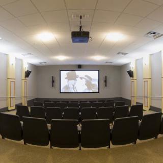 An empty auditorium with rows of seats facing a large projector screen.