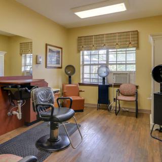 A cozy hair salon interior featuring salon chairs, dryer stations, and a large window with natural light.