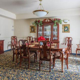 A traditional dining room with a wooden table and chairs, ornate carpet, and chandelier.