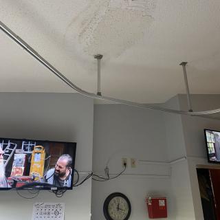 Ceiling with water damage and mounted televisions in a room.