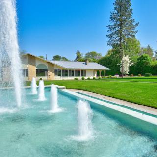 A beautiful house with a large fountain and well-manicured lawn under a clear blue sky.
