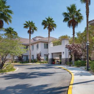 A residential building with palm trees lining the driveway on a sunny day.