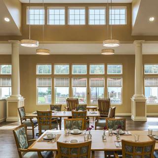 A well-lit dining area with tables and chairs arranged under large windows.