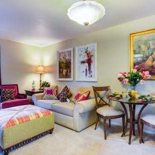 A cozy living room featuring a stylish sofa, decorative artwork, and a small dining table adorned with fresh flowers.