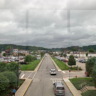 A view of a quiet road lined with greenery, leading towards distant hills under a cloudy sky.