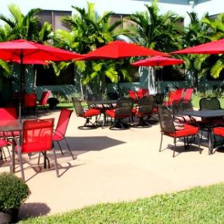 Outdoor patio area with red umbrellas and seating amidst tropical plants.
