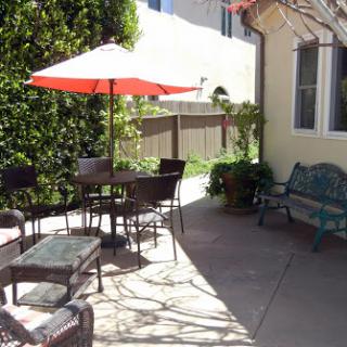 A cozy outdoor patio area with a table, chairs, and a bright red umbrella providing shade.