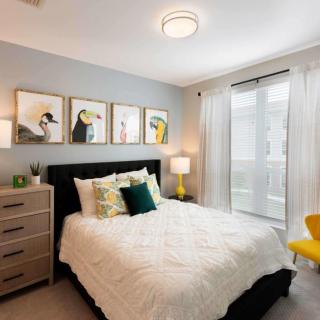 A modern bedroom with stylish decor, featuring a comfortable bed, wall artwork, and ample natural light.