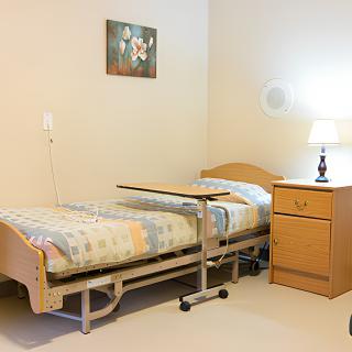 A simple room with a hospital bed, nightstand, and lamp.