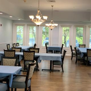 A well-lit dining room with neatly arranged tables and chairs, featuring chandeliers and large windows.
