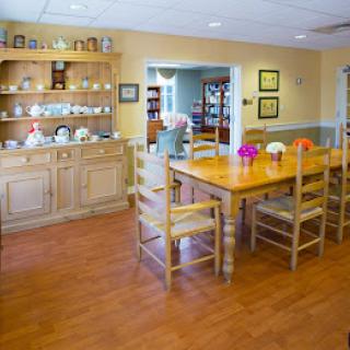 A cozy dining room with a wooden table and chairs, surrounded by decorative dishes and cups on a cupboard.