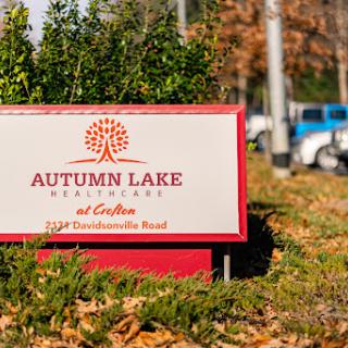 A welcoming sign for Autumn Lake, surrounded by greenery and an autumn backdrop.