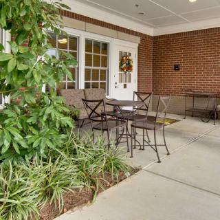A cozy outdoor patio setup with chairs and a table next to lush greenery and a brick wall.