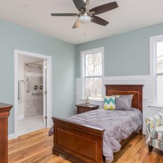 A cozy bedroom with a wooden bed and hardwood flooring, featuring a ceiling fan and adjacent bathroom.