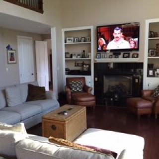 A cozy living room with a television above the fireplace, comfortable seating, and decorative shelving.
