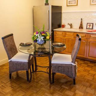 A cozy dining area with a glass top round table and wicker chairs, featuring a floral centerpiece.