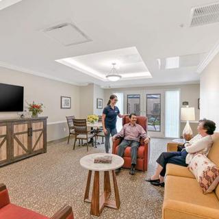 A cozy living room with seniors engaging in conversation with a caregiver, surrounded by comfortable furniture and a large television.