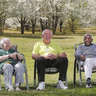 Three seniors sitting on chairs in a grassy area with trees in the background.