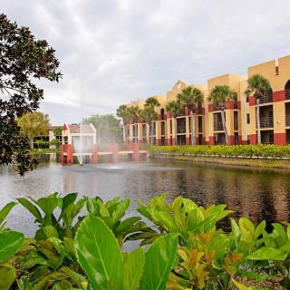 A serene view of a resort with a fountain by the water and lush greenery.