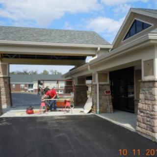 A newly constructed building with a covered driveway, featuring stone accents and workers in the background.