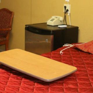 A hotel room featuring a red bedspread, a wooden tray, a telephone on top of a mini fridge.