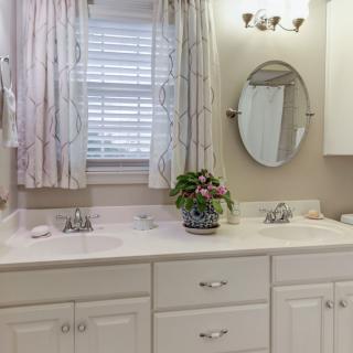 A clean and bright bathroom featuring double sinks, a round mirror, and elegant light fixtures.