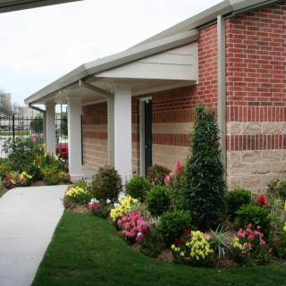 A landscaped area with flowers and bushes alongside a brick building.