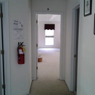 A view of a hallway with doors leading to rooms, featuring a fire extinguisher mounted on the wall.