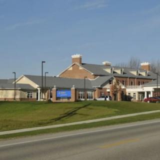 A large brick building with a pitched roof sits beside a road under a clear blue sky.