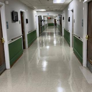 A wide view of a hospital corridor with multiple doors leading to patient rooms.