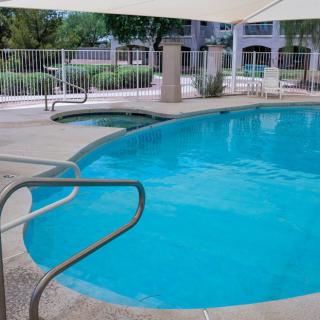 An outdoor swimming pool surrounded by a fence, with clear water on a sunny day.