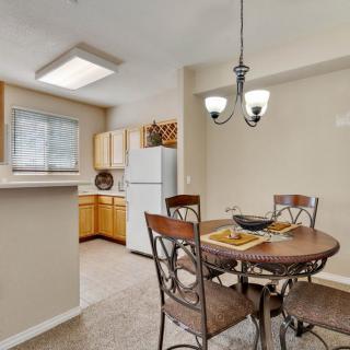 A cozy kitchen and dining area with a round table, chairs, refrigerator, and wood cabinets.